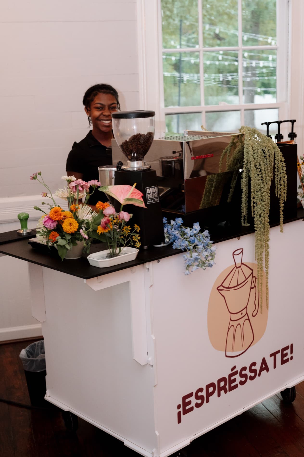 Espréssate barista smiling behind the branded mobile espresso bar, styled with florals at a Triangle wedding venue