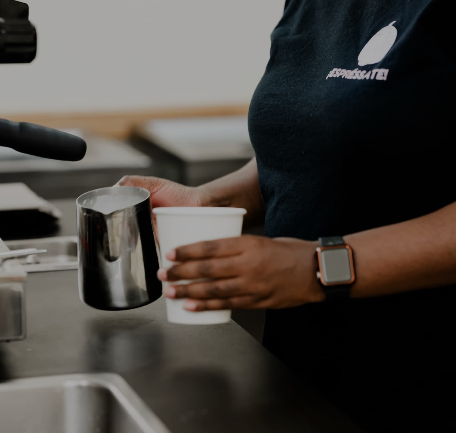 Espréssate barista in a branded shirt pouring steamed milk into a cup at a catered event
